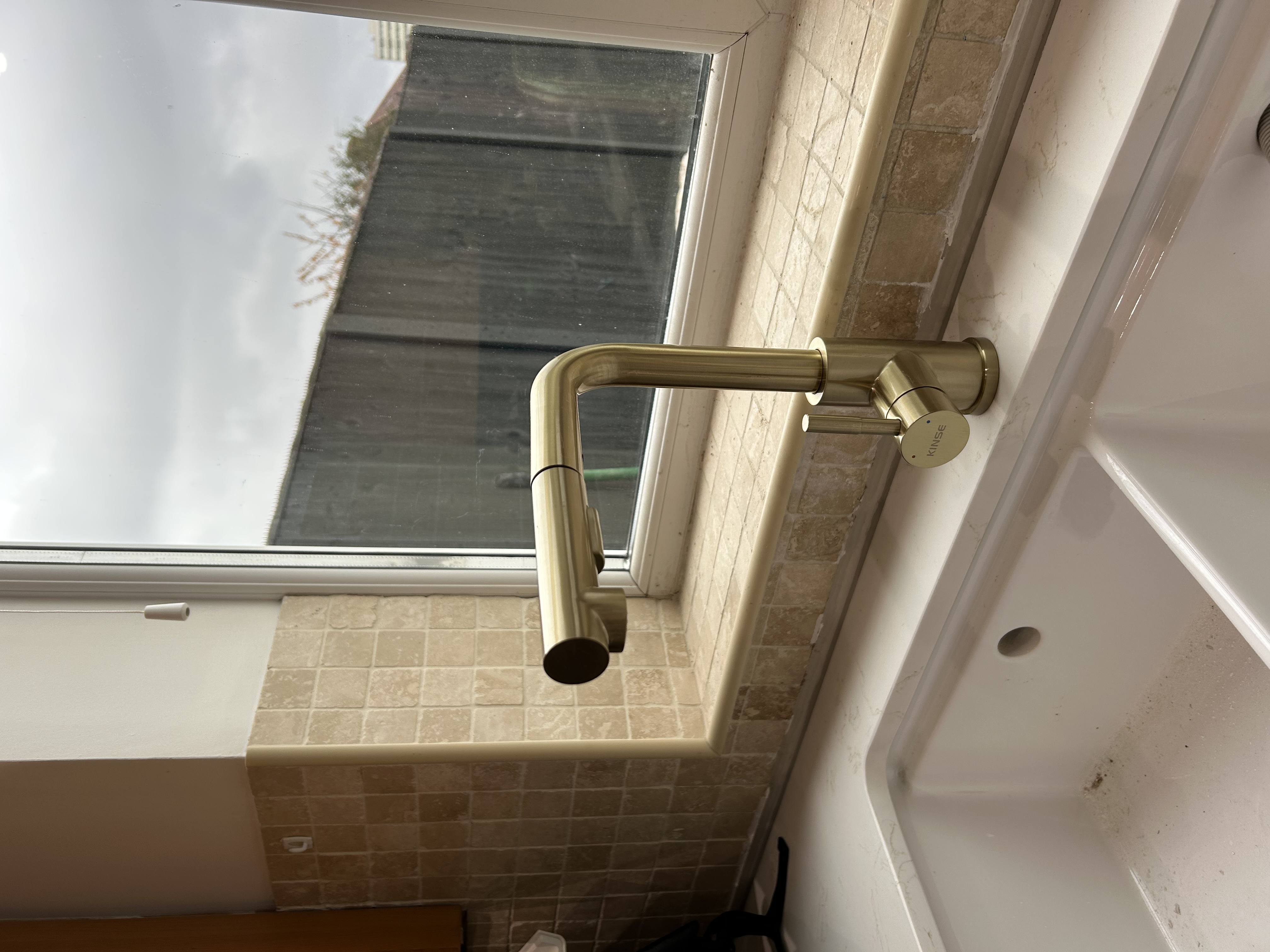 Gold brass tap installed in tiled bathroom